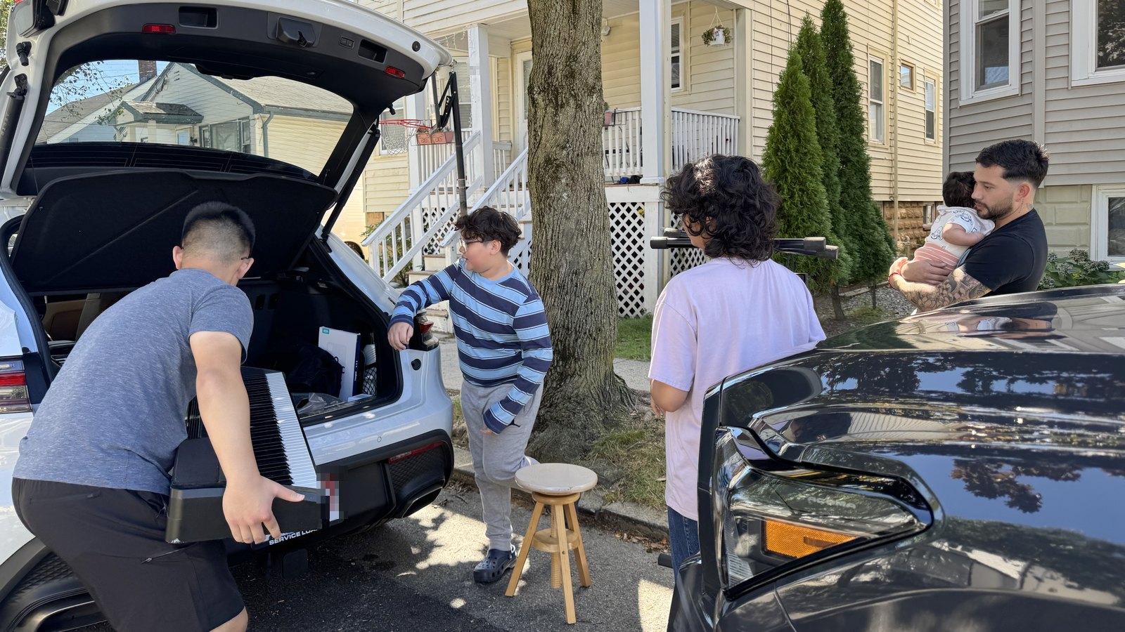 A student lifting a keyboard off the tailgate while the family it is going to waits on the sidewalk.