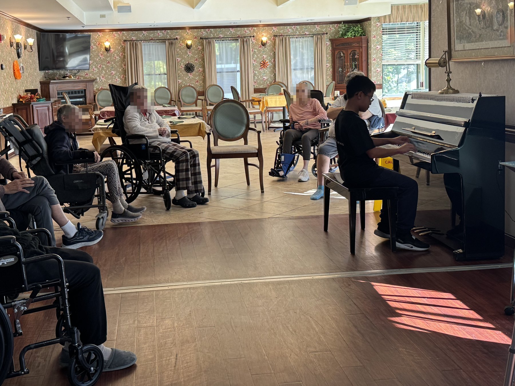 A student playing an upright piano for residents in a dining room.