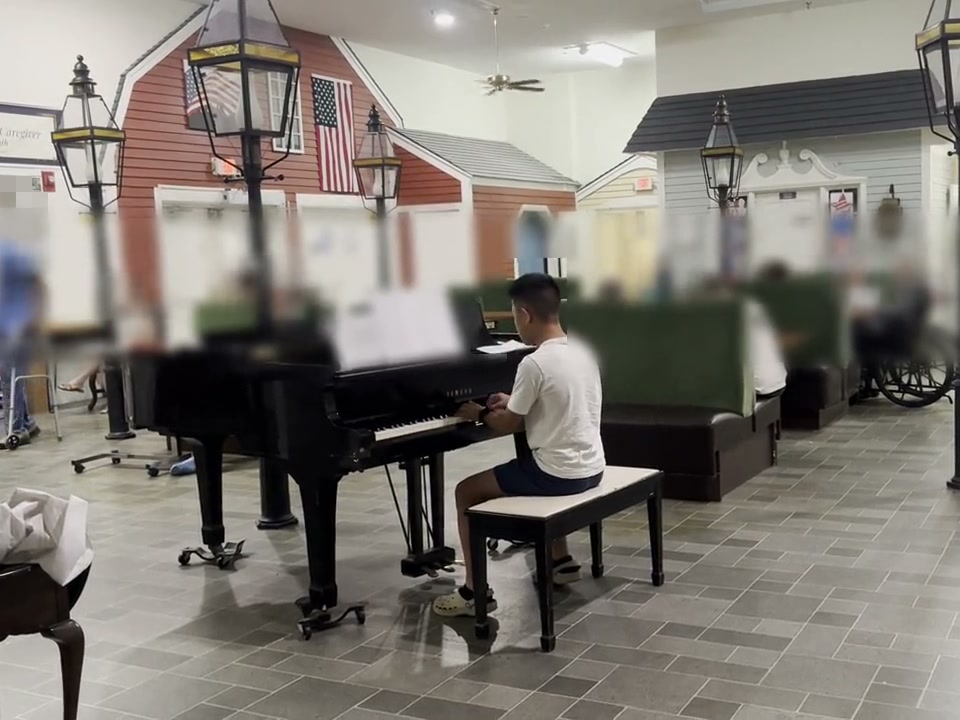 A student in a white shirt playing a grand piano for residents.