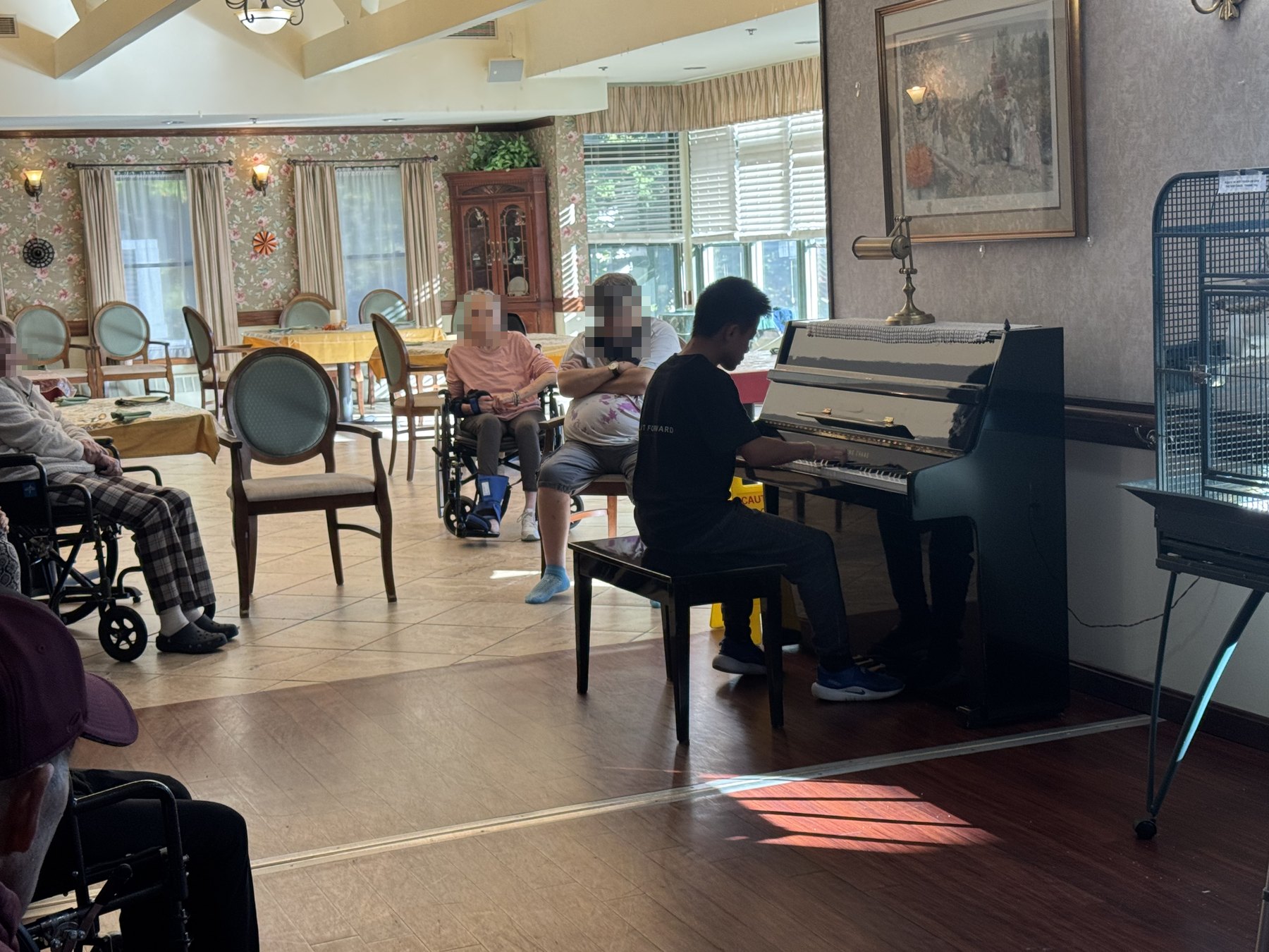 A student at the piano with residents listening nearby.