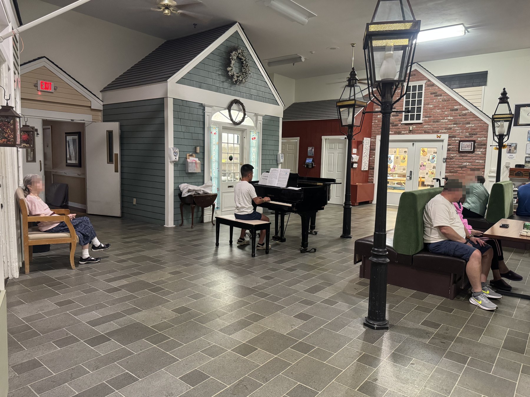 A student at the piano in a residence common room, with people listening from a chair and from the booths.
