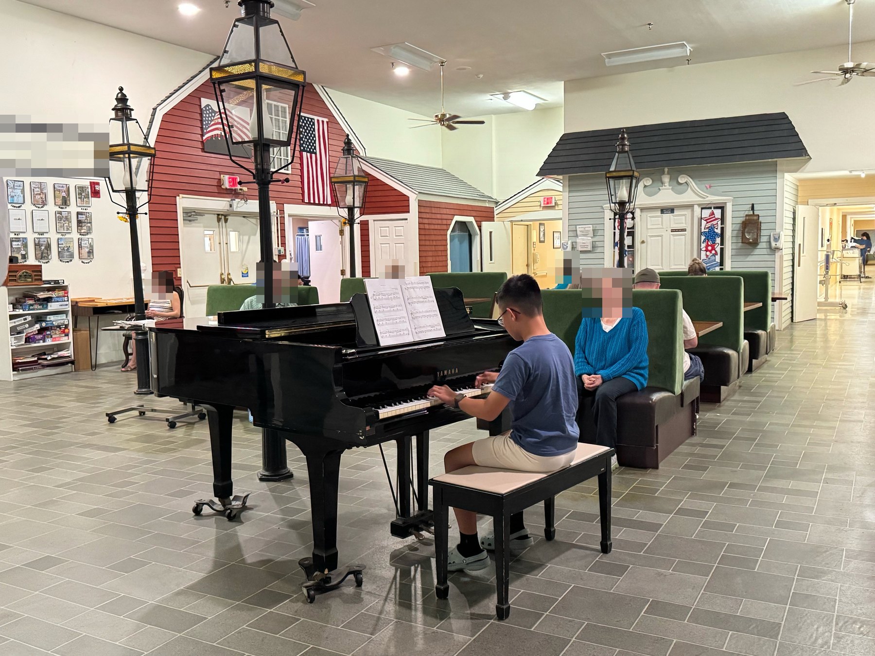 A student playing a grand piano while residents listen from the seating around him.